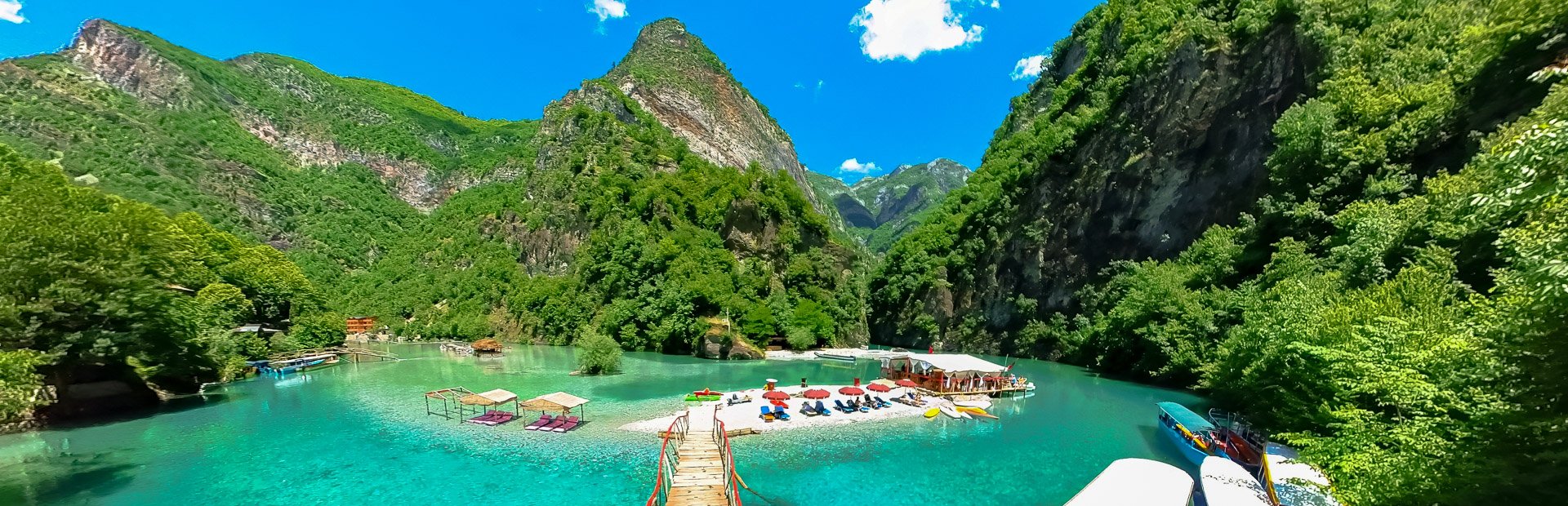 Panoramisch uitzicht in Albanië op een turquoise rivier tussen steile groene bergen met een zandbank met ligbedden en een pier