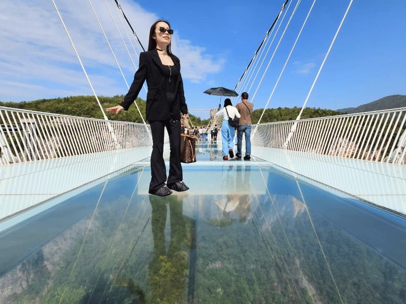 Vrouw poseert op de glazen brug met natuur op de achtergrond