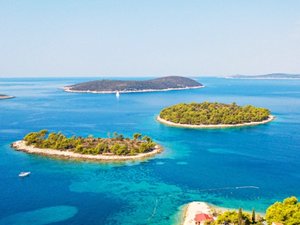 Meerdere groene eilanden in een helderblauwe zee met boten onder een stralende lucht in Kroatië