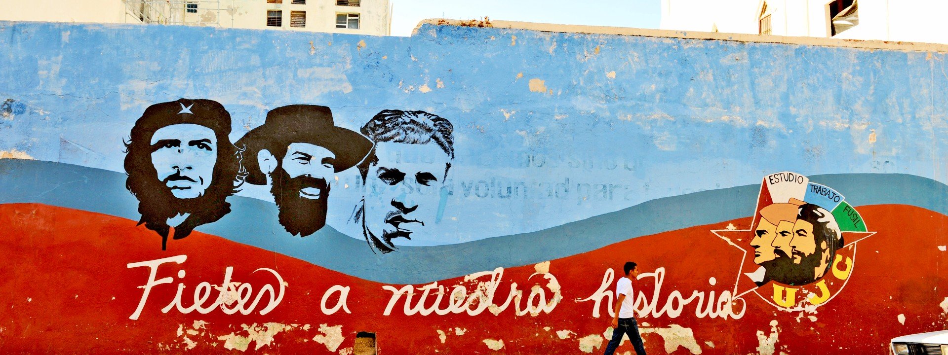 Verweerde muurschildering met portretten van Che Guevara, Camilo Cienfuegos en een andere revolutionaire figuur, met de tekst “Fieles a nuestra historia” en een UJC-embleem.