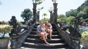 Een gezin van vier zit op stenen trappen met drakenleuningen bij een sfeervolle watertuin op Bali, Indonesië.
