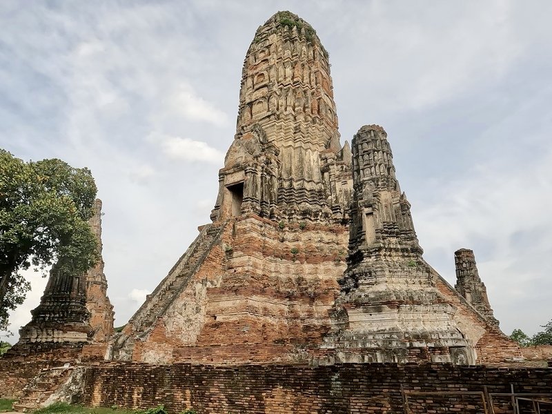 Verweerde bakstenen tempeltoren uit het oude Ayutthaya-rijk. Trappen leiden naar een heiligdom bovenin, omgeven door kleinere torens. Het geheel straalt historie en vergankelijkheid uit.