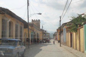 Straat in oud Trinidad met kleurrijke gebouwen, elektriciteitspalen, voetgangers en een blauwe auto op een kasseienweg in Cuba