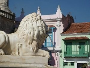 Witte marmeren fontein met leeuw die water spuwt met roze en groene gebouwen op de achtergrond in Cuba