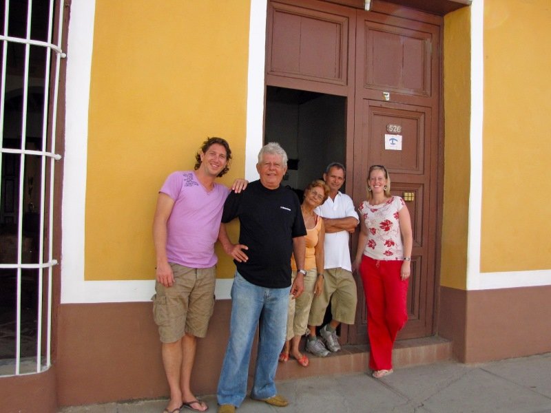 Vijf volwassenen poseren voor een geel gebouw met een bruine deur in Cuba