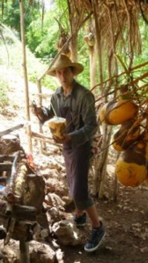 Man met strohoed houdt een kokosnoot en machete vast in een rustieke buitenomgeving met gele kokosnoten in Cuba