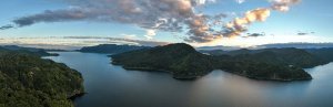 Panoramisch uitzicht op een uitgestrekt meer omringd door weelderige beboste bergen onder een dramatische zonsondergang in een bergachtig natuurgebied