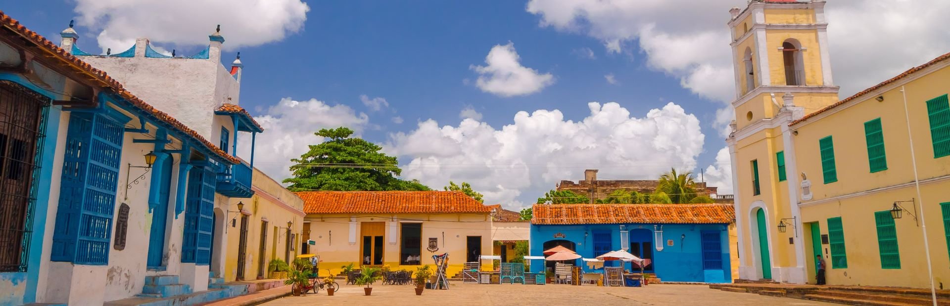 Levendig koloniaal dorpsplein met kleurrijke gebouwen, blauwe luiken en een kerktoren in Cuba