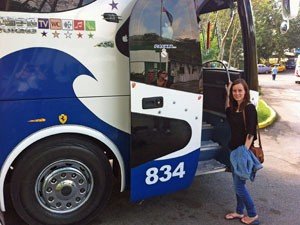 Lachende vrouw staat naast een open deur van een blauw-witte bus in Cuba