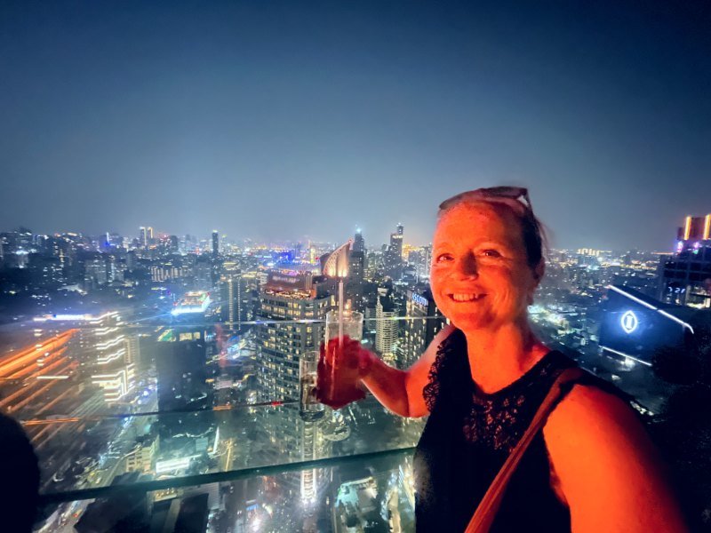 Vrouw met een drankje op rooftop, met uitzicht op verlichte stad bij nacht.