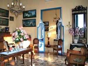 Sfeervol ingerichte antieke kamer met kroonluchter, schilderijen, bloemstukken en gedecoreerde vloertegels in zonlicht in Cuba