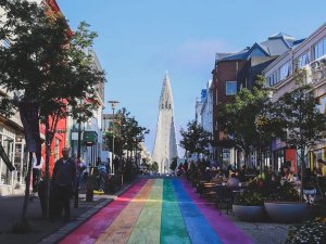 Regenboogstraat leidt naar een hoge witte kerk met gebouwen, terrassen en mensen aan weerszijden in Reykjavik in IJsland