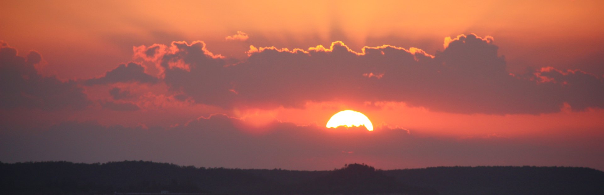 Oranje-rode zonsondergang met de zon deels achter de wolken boven een donker landschap in Cuba