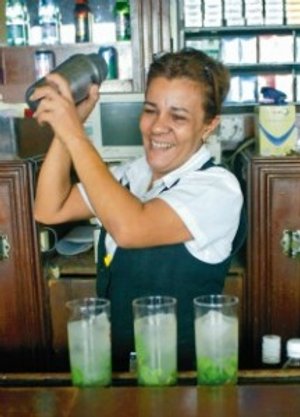 Lachende vrouwelijke bartender schudt een cocktailshaker achter de bar met drie mojito’s in Havana in Cuba