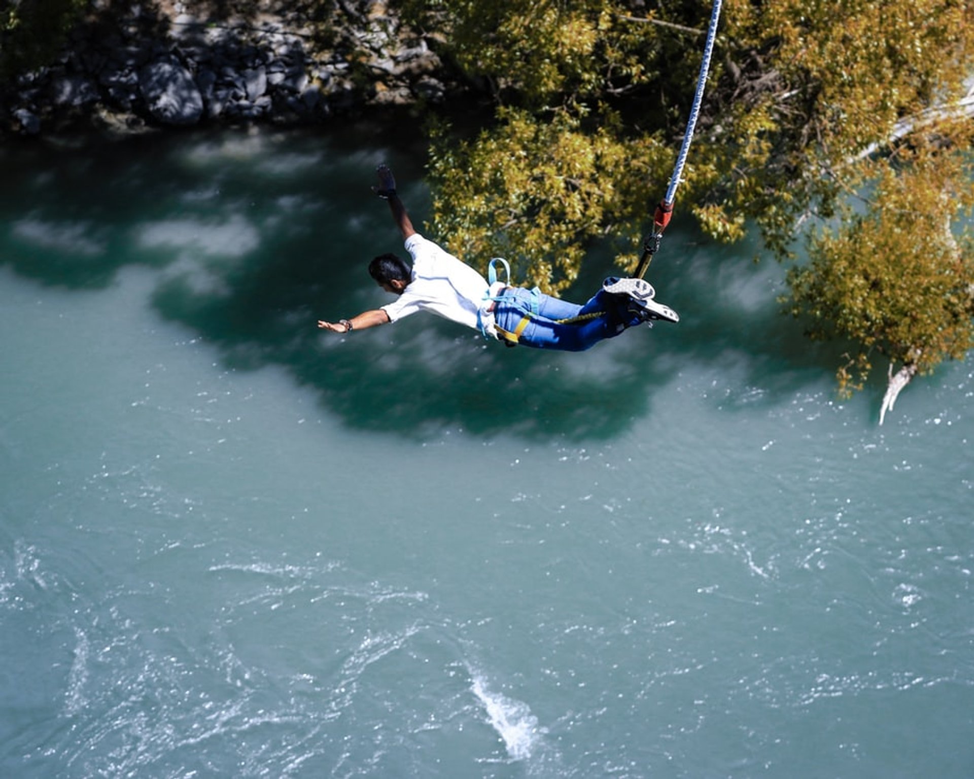 Persoon maakt een bungeejump met het hoofd naar beneden richting een turquoise rivier en veroorzaakt een grote plons in een avontuurlijk natuurgebied