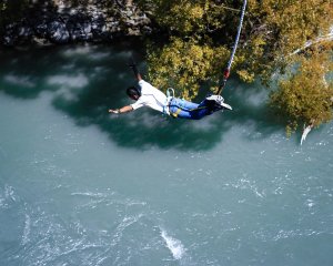 Persoon maakt een bungeejump met het hoofd naar beneden richting een turquoise rivier en veroorzaakt een grote plons in een avontuurlijk natuurgebied