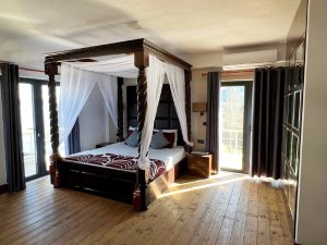 Lichte slaapkamer bij het Ohridmeer in Noord-Macedonië met donker houten hemelbed, witte gordijnen en balkondeuren