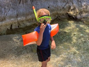 Kind met snorkelset en zwembandjes in helder ondiep water bij een rotsachtige kust in Kroatië