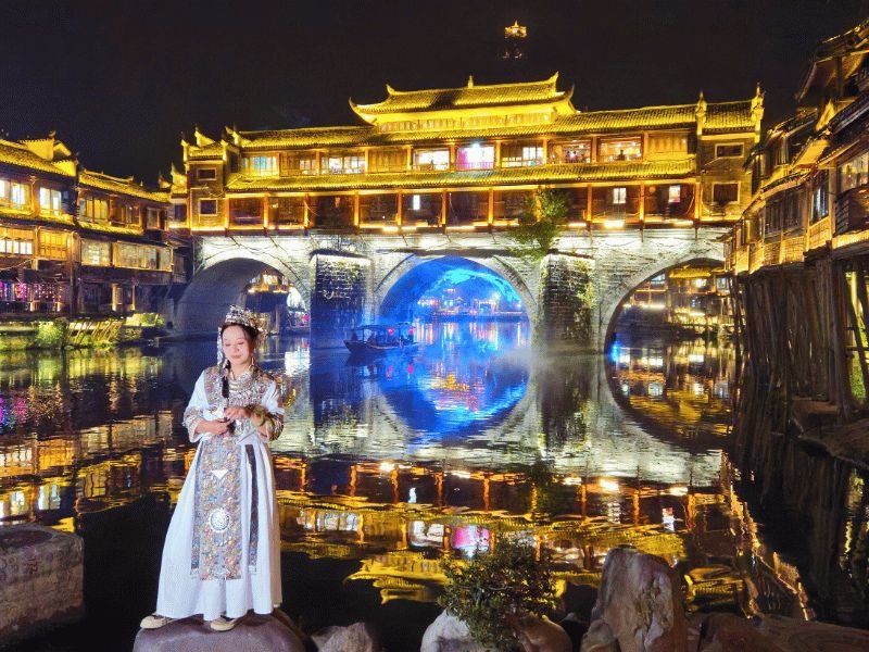 Vrouw poseert voor water met verlicht gebouwen op de achtergrond