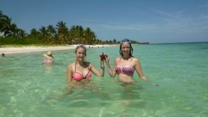 Twee vrouwen in bikini houden een zeester vast in helder zeewater op een zonnig strand met palmbomen bij Cayo Levisa in Cuba