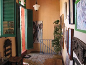 Kleurrijke gang met open groene luiken tegelvloer kunst aan de muur en blauwe trapleuning in casa particular in Trinidad Cuba
