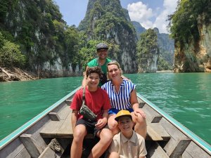 Een lachend gezin van vier in een boot op turquoise water, omringd door hoge kalkstenen rotsformaties in Thailand.