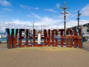 Vrouw poseert achter grote WELLINGTON letters bij een zonnige jachthaven aan de waterkant in Wellington Nieuw-Zeeland