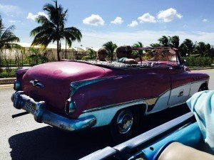 Roze-witte vintage cabrio met passagiers op een zonnige dag in Cuba