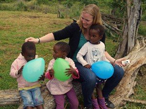 Lachende vrouw en drie jonge kinderen zitten op een boomstam en houden allemaal een ballon vast in Zuid-Afrika