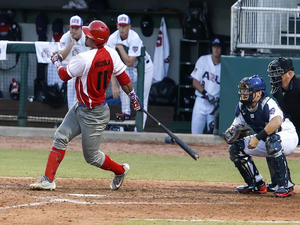 Honkballer in rood uniform slaat de bal terwijl catcher en scheidsrechter achter hem staan in Cuba