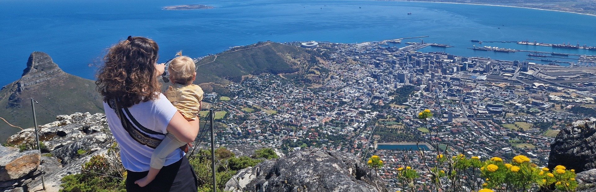 Vrouw met baby kijkt uit over het panoramische uitzicht op Kaapstad, de oceaan en de Lion’s Head-berg in Zuid-Afrika