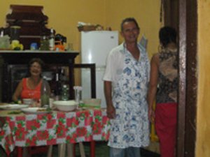Glimlachende man met schort staat in een keuken terwijl een vrouw aan tafel zit en een andere vrouw deels zichtbaar is in Havana Cuba