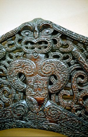 Gedetailleerd Māori houtsnijwerk van een gestileerde figuur met spiraalpatronen in een culturele setting in Nieuw-Zeeland