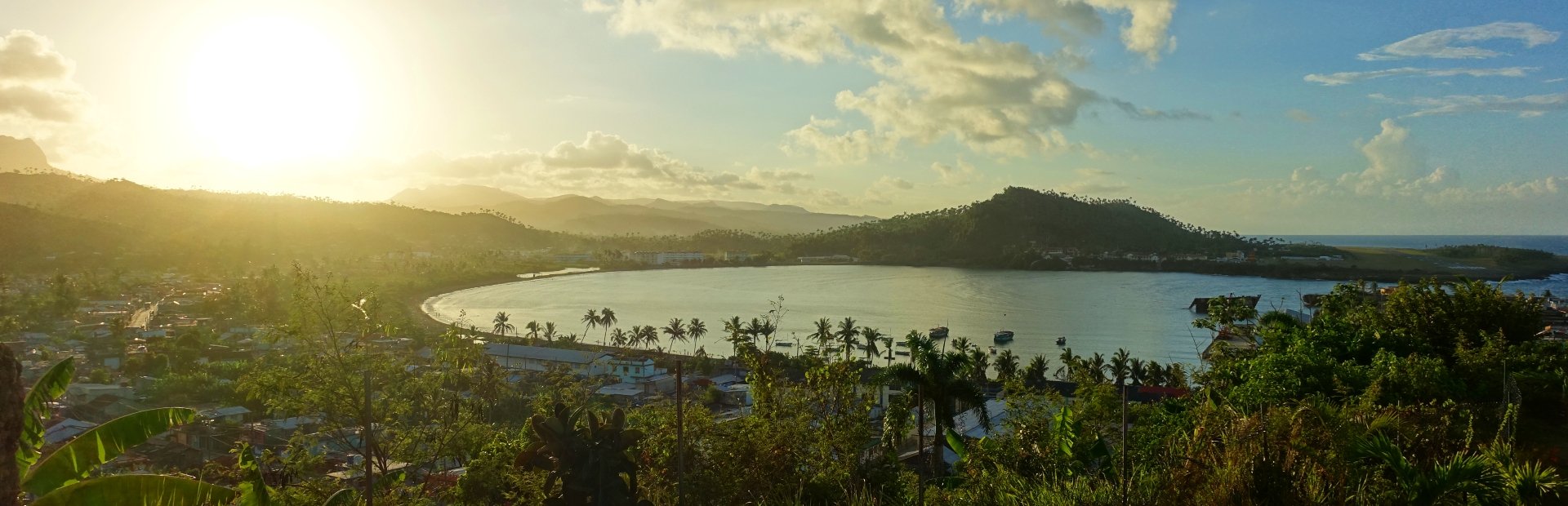 Panoramisch uitzicht op een stadje rond een tropische baai met weelderige heuvels onder een gouden zonsondergang in Cuba