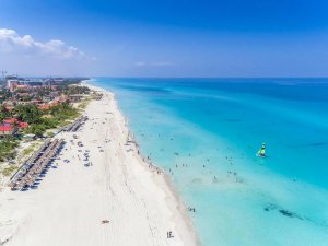 Luchtfoto van een lang wit zandstrand in Cuba met turquoise water, mensen en rieten parasols.