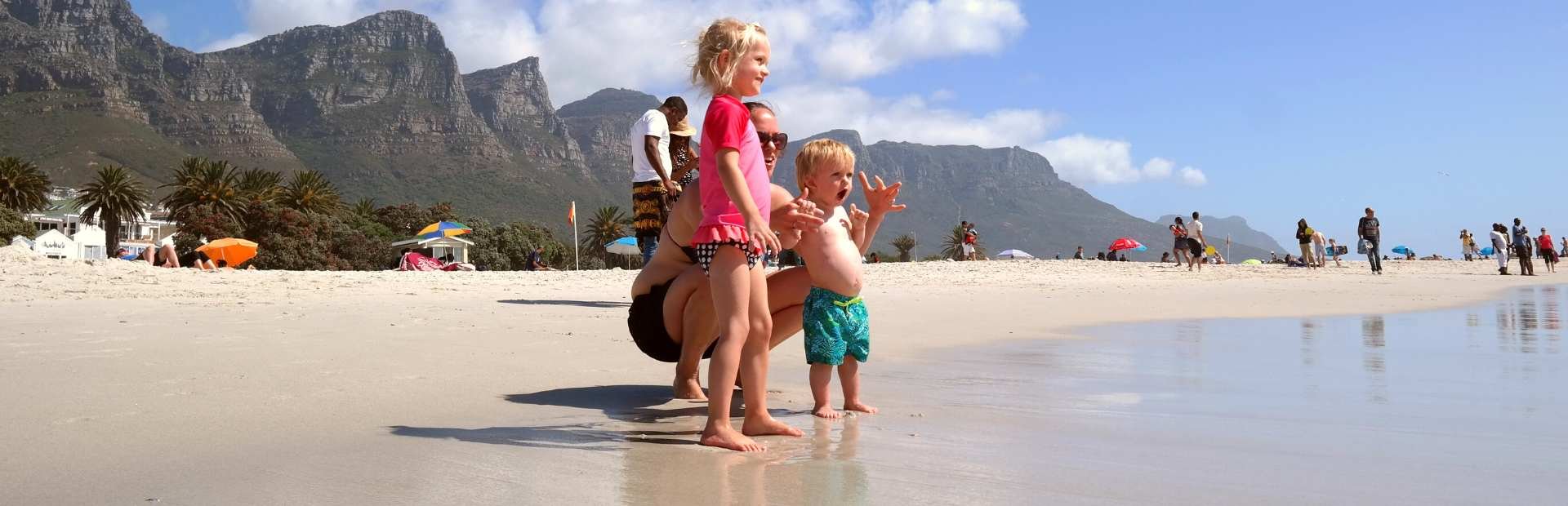 Moeder met twee jonge kinderen op een zonnig strand, met bergen op de achtergrond in Zuid-Afrika