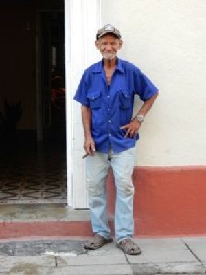 Lachende oudere man in een blauw shirt, pet en spijkerbroek houdt een sigaar vast in Cuba
