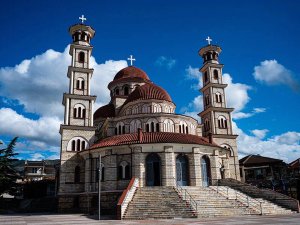 Sierlijke stenen kerk in Albanië met meerdere rode koepels en twee hoge klokkentorens onder een blauwe lucht