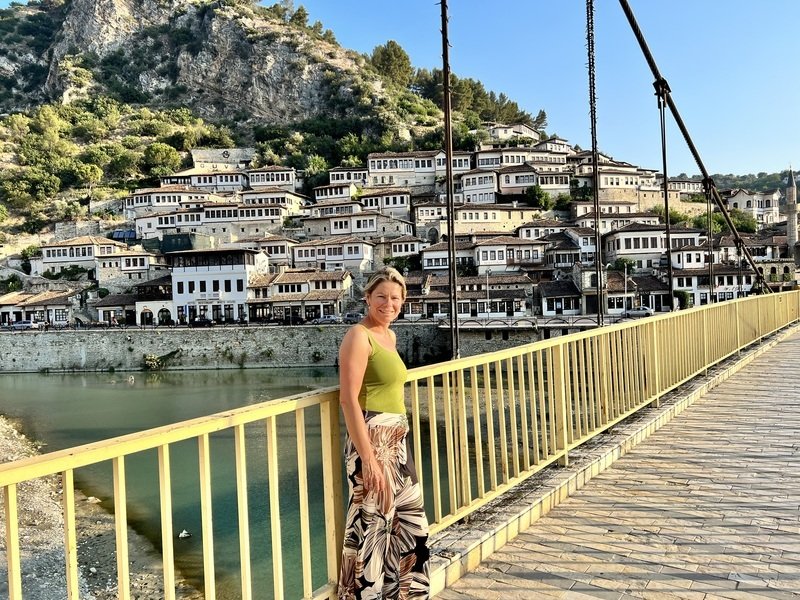 Vrouw glimlacht op gele brug in Berat met rivier en witte huizen tegen berg, Albanië