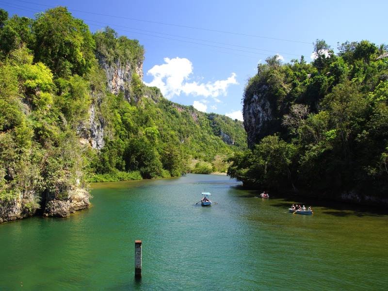 Boten op een groene rivier die tussen weelderige, rotsachtige kliffen stroomt onder een blauwe lucht in Cuba