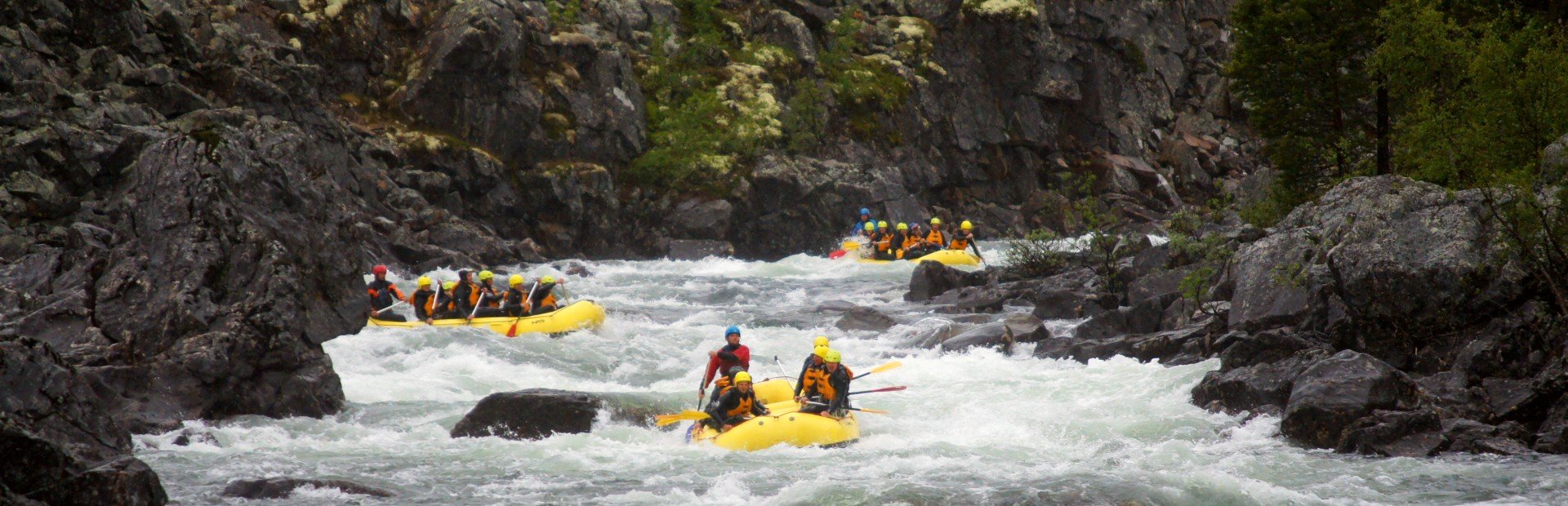 People in yellow rafts navigating white water rapids in a rocky river.