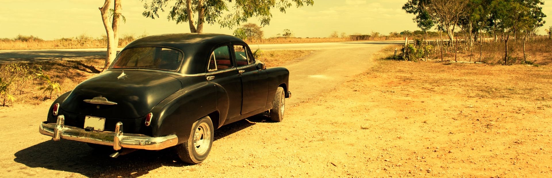 Vintage zwarte auto geparkeerd op een stoffige zandweg in een zonnig landelijk landschap in Cuba