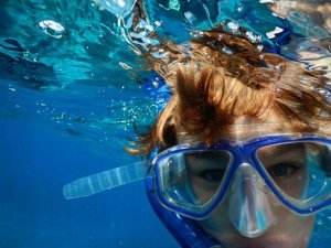 Kind met snorkelmasker onder water, deels boven wateroppervlak.