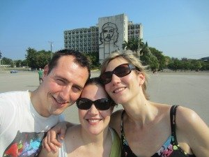 Drie lachende mensen met zonnebril staan voor een gebouw met een grote contour van Che Guevara in Havana in Cuba