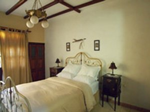 Slaapkamer met wit smeedijzeren bed houten meubels en balkenplafond in casa particular in Trinidad Cuba