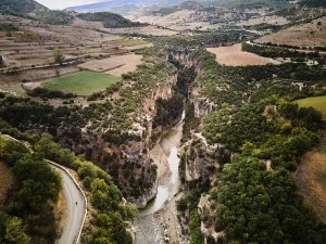 Luchtfoto van rivier door diepe, met bomen begroeide kloof met akkers, heuvels en een kronkelende weg in Osum Canyon, Berat, Albanië
