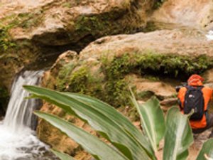Persoon met oranje jas en zwarte rugzak maakt een foto van een waterval in Topes de Collantes Cuba