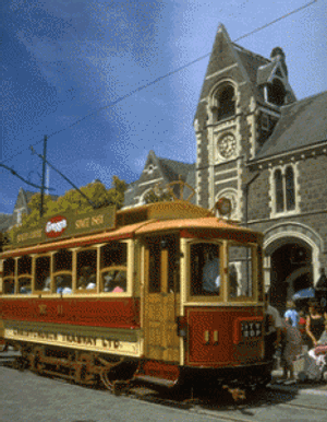 Vintage rood crèmekleurige Christchurch Tramway tram met passagiers voor een historisch stenen gebouw met klokkentoren in Christchurch Nieuw-Zeeland