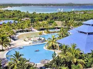 Luchtfoto van een tropisch resort met blauwgekleurde daken, kronkelende zwembaden, palmbomen en zee met zeilboten bij Playa Pesquero in Cuba