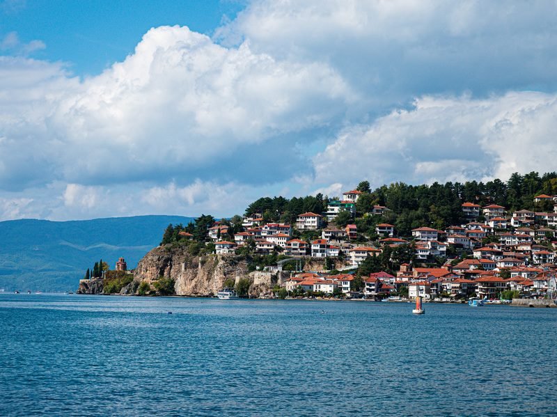 Stadje aan het Ohridmeer in Noord-Macedonië met rode daken op een heuvel, een kerk op de klif en boten op het water